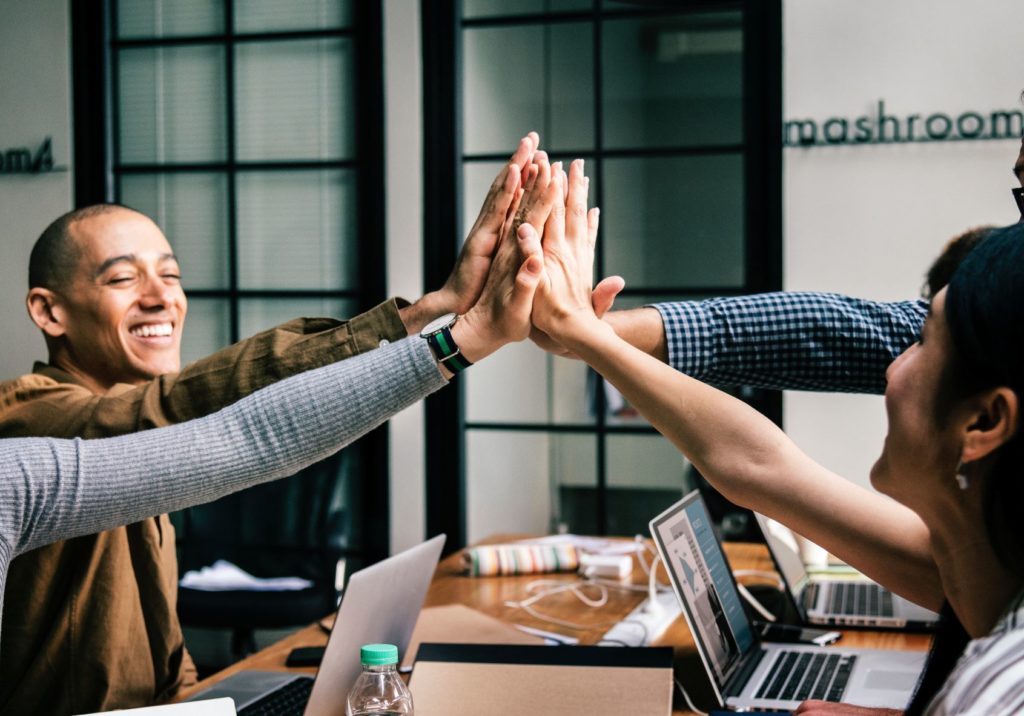 Four people high-fiving eachother around a work table.