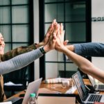 Four people high-fiving eachother around a work table.