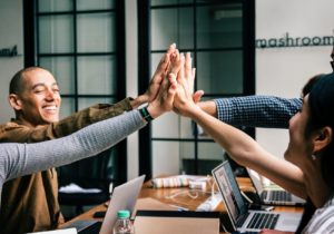 Four people high-fiving eachother around a work table.